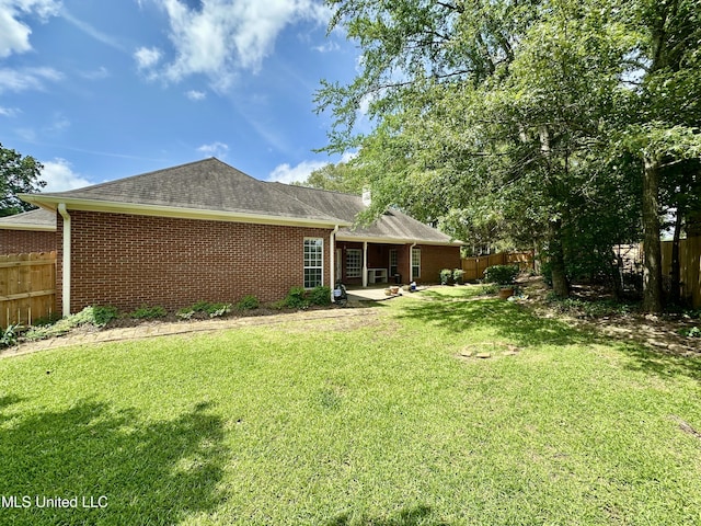 back of property with a yard, brick siding, a shingled roof, and fence