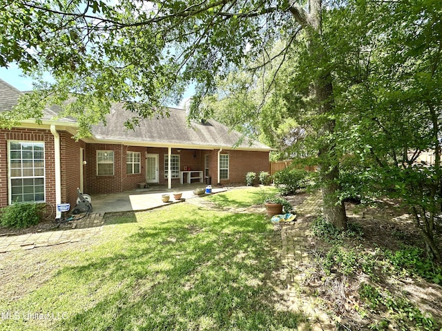 rear view of house with a patio, a shingled roof, brick siding, and a lawn