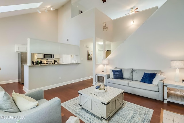 living room with dark wood-style floors, a skylight, ceiling fan, and baseboards