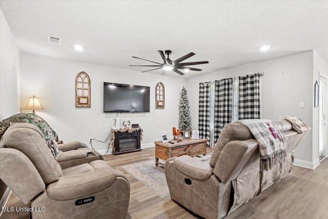 living room with visible vents, light wood-type flooring, a ceiling fan, and a glass covered fireplace