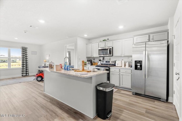 kitchen featuring light wood finished floors, stainless steel appliances, an island with sink, and baseboards