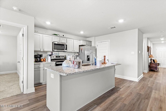 kitchen featuring baseboards, visible vents, an island with sink, appliances with stainless steel finishes, and light wood-type flooring