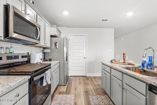 kitchen with visible vents, light stone counters, appliances with stainless steel finishes, light wood-style floors, and a sink