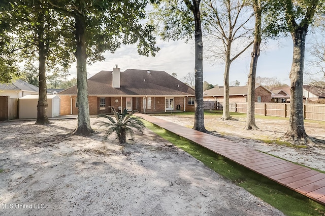 rear view of property with brick siding, a chimney, and fence