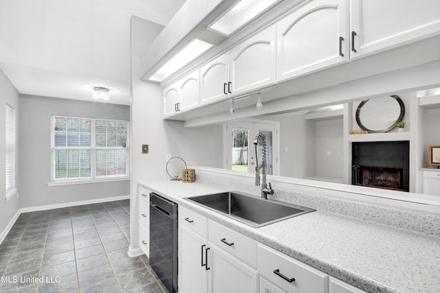 kitchen featuring dishwashing machine, white cabinets, and a sink