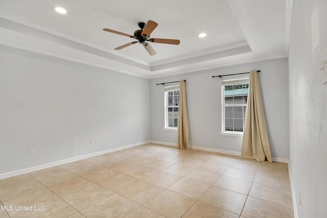 empty room with a textured ceiling, a tray ceiling, baseboards, and ornamental molding