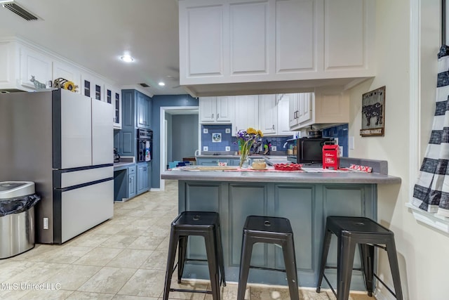 kitchen with kitchen peninsula, stainless steel refrigerator, white cabinetry, and a breakfast bar