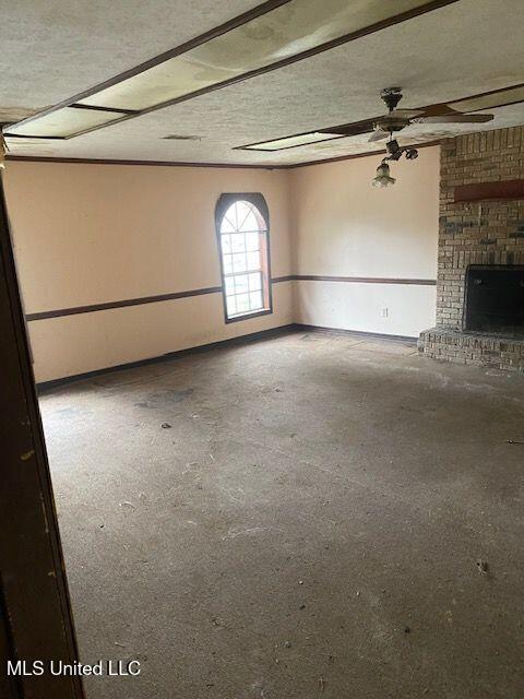 interior space with ceiling fan, concrete flooring, a textured ceiling, and a brick fireplace