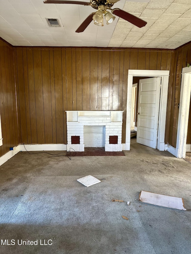 unfurnished living room featuring ceiling fan, a fireplace, carpet floors, and wood walls