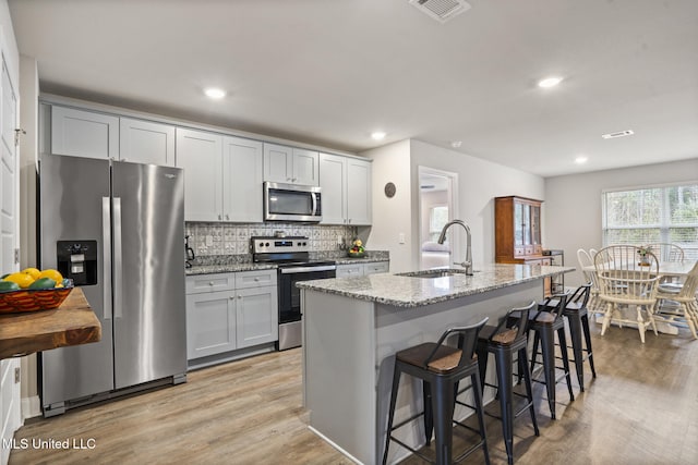 kitchen featuring light stone counters, stainless steel appliances, tasteful backsplash, light wood-style floors, and a sink