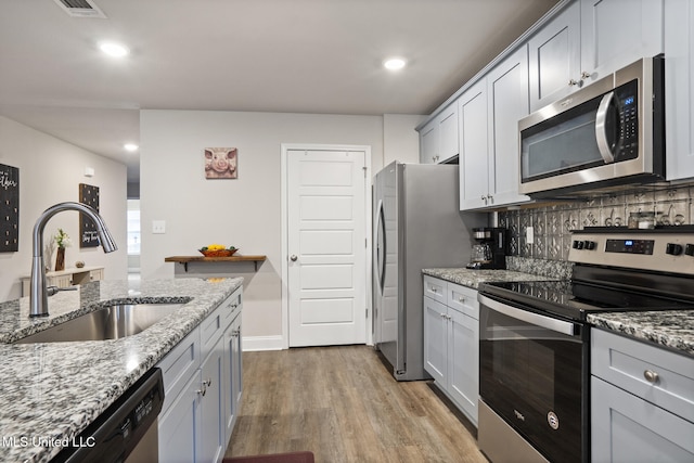 kitchen featuring decorative backsplash, appliances with stainless steel finishes, light stone countertops, light wood-style floors, and a sink