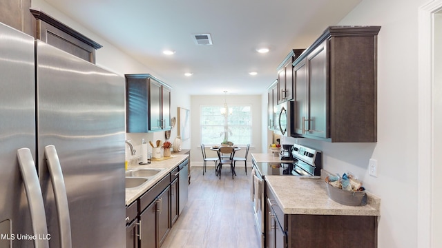 kitchen featuring appliances with stainless steel finishes, dark brown cabinetry, pendant lighting, and light hardwood / wood-style floors