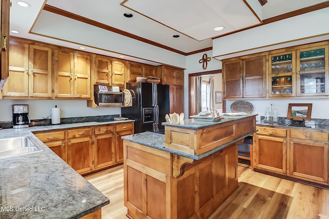 kitchen with black fridge, crown molding, light wood-type flooring, a kitchen island, and a kitchen bar