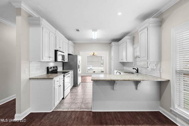 kitchen featuring appliances with stainless steel finishes, a breakfast bar, a peninsula, white cabinetry, and a sink