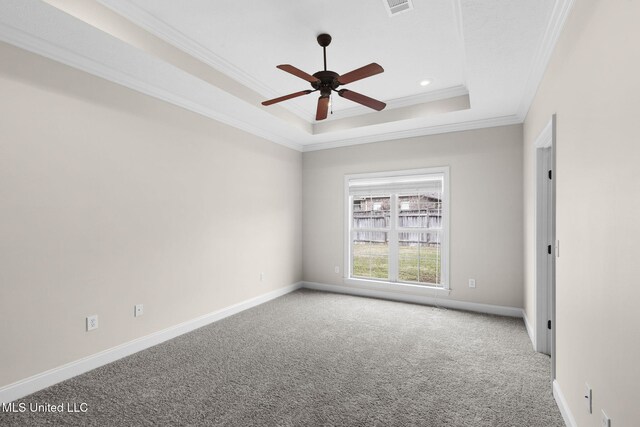 empty room with ceiling fan, carpet floors, baseboards, ornamental molding, and a raised ceiling