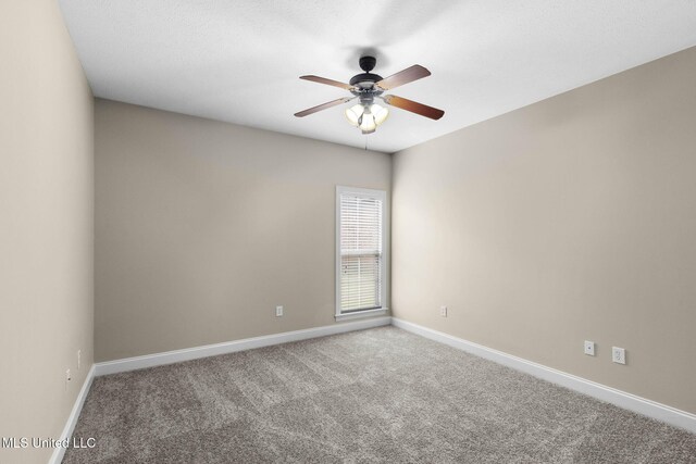 carpeted spare room featuring baseboards and a ceiling fan