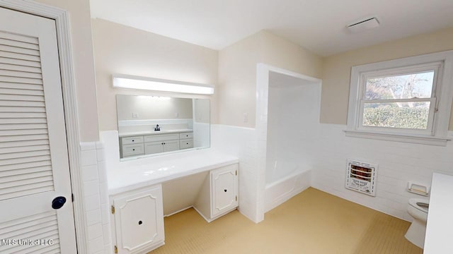 bathroom featuring heating unit, a tub, toilet, and vanity