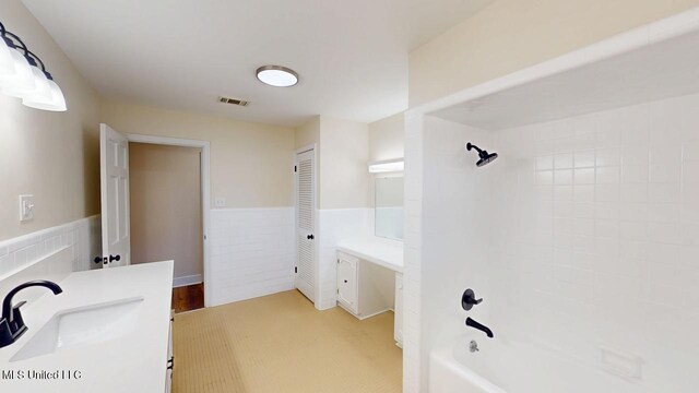 full bath featuring a wainscoted wall, visible vents, shower / bathing tub combination, and vanity