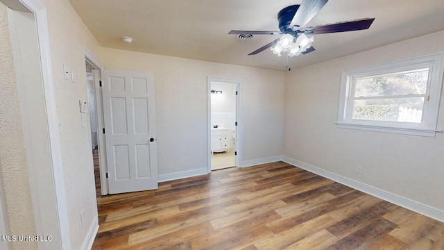 unfurnished bedroom with ceiling fan, ensuite bath, baseboards, and wood finished floors