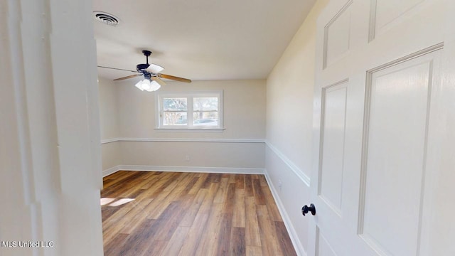 unfurnished room with a ceiling fan, visible vents, baseboards, and wood finished floors