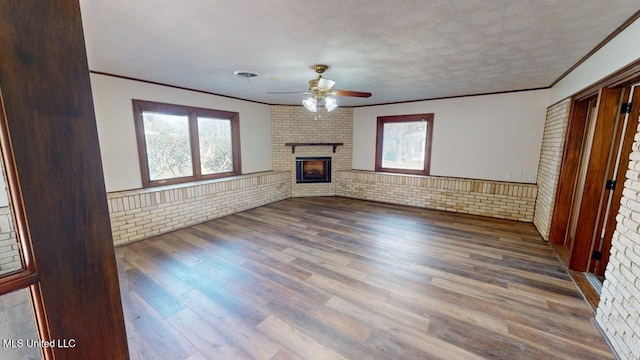 unfurnished living room with brick wall, a brick fireplace, wood finished floors, and a wealth of natural light