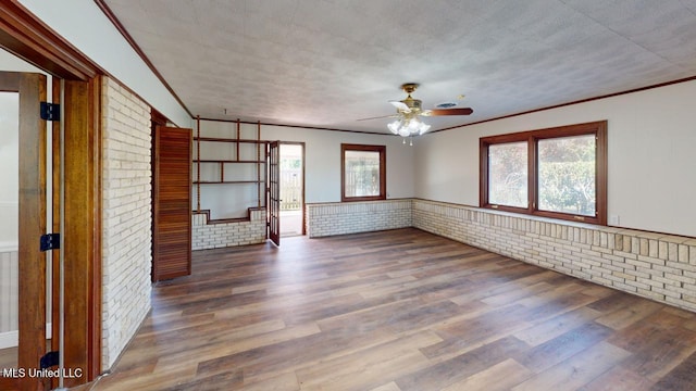 unfurnished living room featuring wainscoting, plenty of natural light, brick wall, and wood finished floors