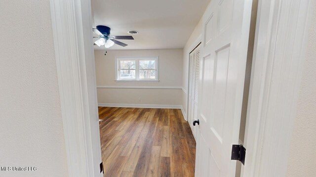 unfurnished bedroom with two closets, ceiling fan, baseboards, and wood finished floors