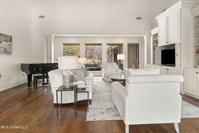 living area with dark wood-style flooring, a towering ceiling, and baseboards