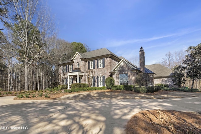 view of front of house with driveway, brick siding, and a chimney