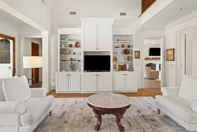 living room with visible vents, light wood-style flooring, a fireplace, and a towering ceiling