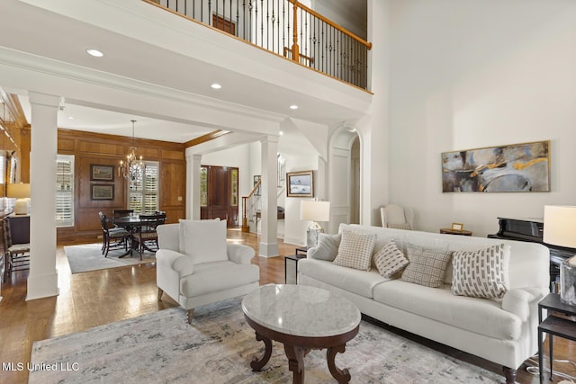 living area with stairway, a high ceiling, an inviting chandelier, wood finished floors, and ornate columns