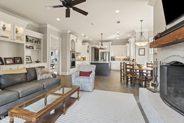 living room featuring a large fireplace, ceiling fan with notable chandelier, dark tile patterned floors, visible vents, and ornamental molding