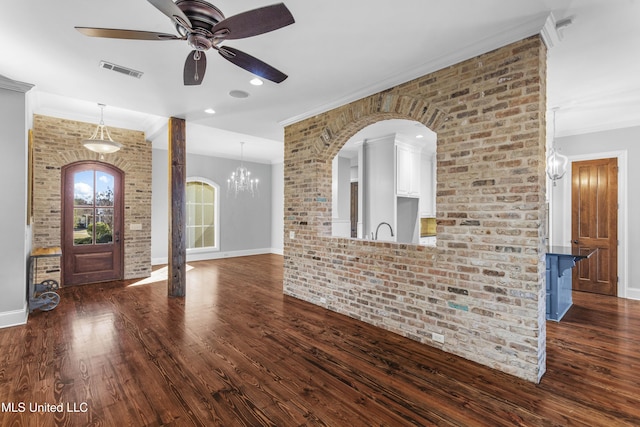 unfurnished living room featuring ornamental molding, brick wall, dark hardwood / wood-style floors, and ceiling fan with notable chandelier