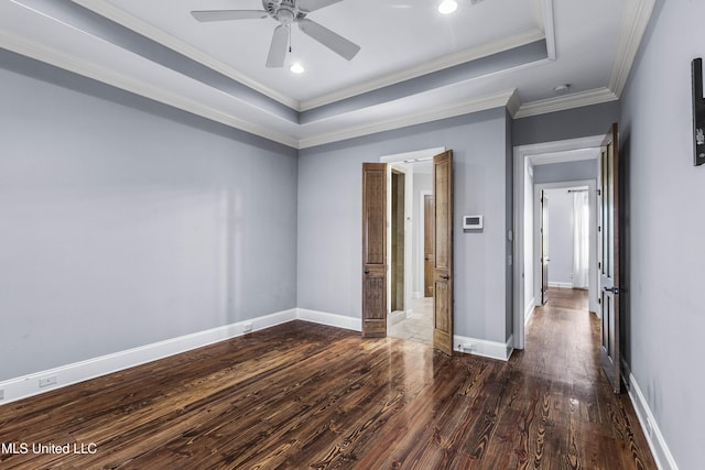 empty room featuring dark wood-type flooring, ceiling fan, ornamental molding, and a tray ceiling