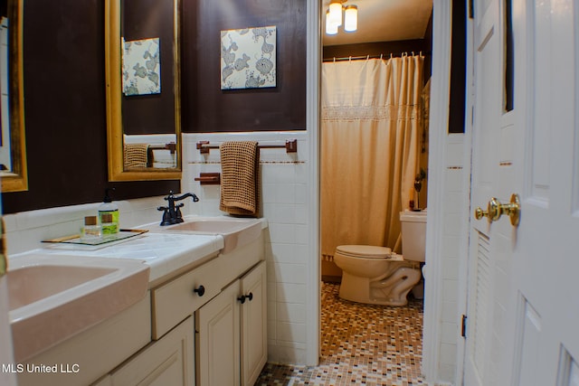 full bathroom featuring tile walls, double vanity, toilet, wainscoting, and a sink