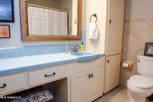 bathroom with toilet, a shower with curtain, tile patterned flooring, vanity, and tile walls