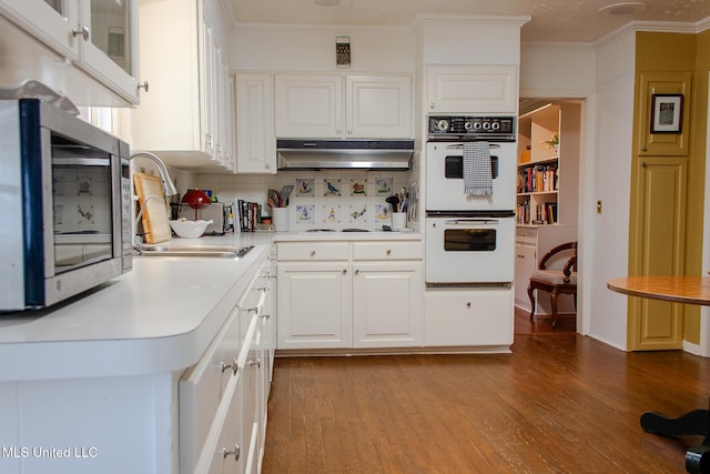 kitchen with under cabinet range hood, white appliances, wood finished floors, a sink, and ornamental molding