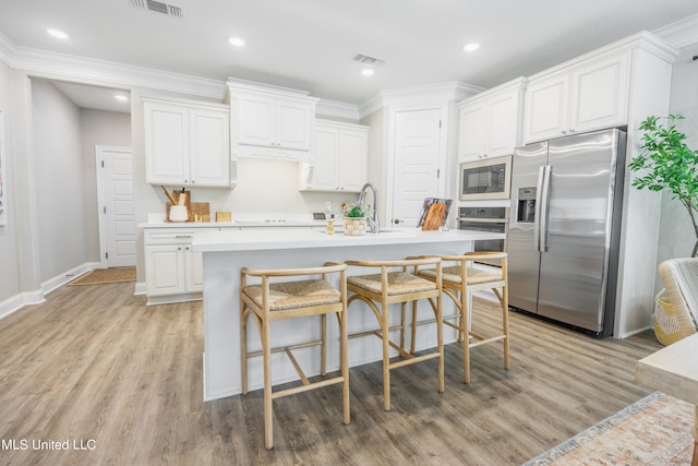 kitchen featuring white cabinetry, appliances with stainless steel finishes, light wood-type flooring, and an island with sink