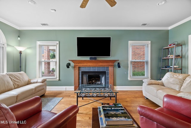 living room featuring crown molding, baseboards, wood finished floors, a fireplace, and ceiling fan
