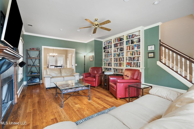 living area featuring a chandelier, wood finished floors, a ceiling fan, crown molding, and baseboards