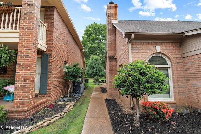 view of side of property with a chimney, roof with shingles, brick siding, and central AC