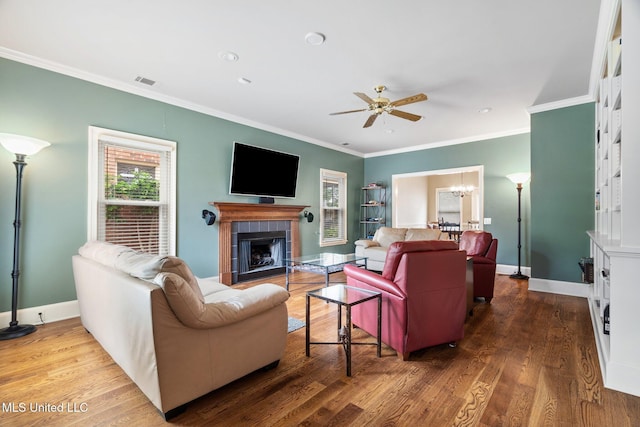 living room featuring a ceiling fan, a tiled fireplace, ornamental molding, a chandelier, and wood finished floors