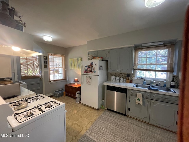 kitchen featuring gray cabinetry, tile counters, sink, white appliances, and decorative backsplash