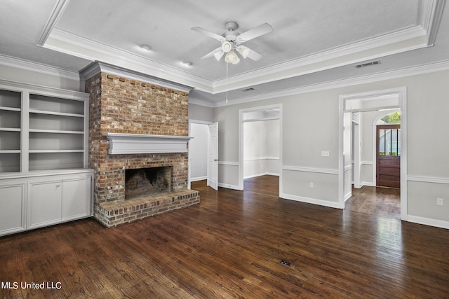 unfurnished living room featuring ceiling fan, a raised ceiling, dark hardwood / wood-style flooring, a brick fireplace, and ornamental molding