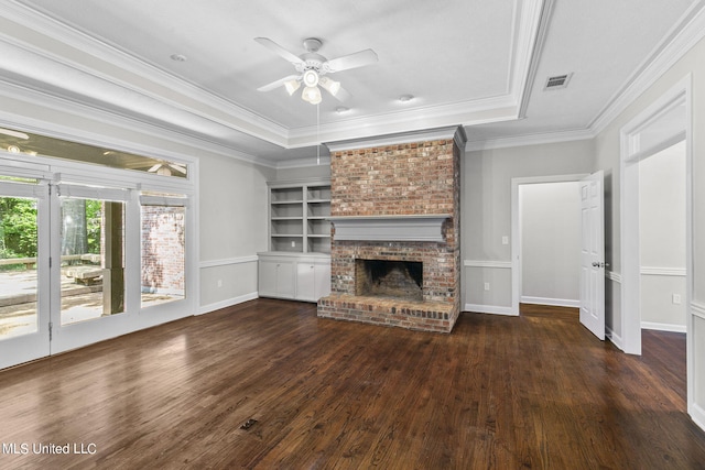 unfurnished living room with ceiling fan, a raised ceiling, a brick fireplace, dark hardwood / wood-style floors, and crown molding