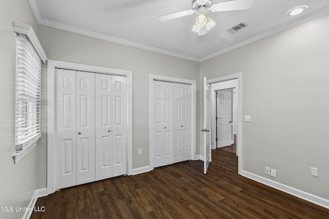 unfurnished bedroom with two closets, dark hardwood / wood-style flooring, ceiling fan, a textured ceiling, and ornamental molding