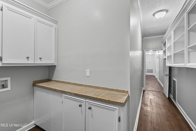 interior space featuring cabinets, washer hookup, a textured ceiling, ornamental molding, and dark wood-type flooring