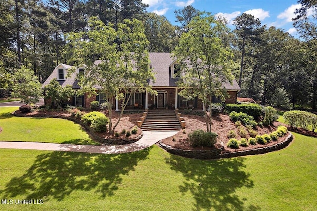 view of front facade featuring brick siding, a shingled roof, a front lawn, and stairs