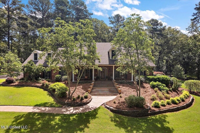 view of front facade featuring stairway, brick siding, a front yard, and roof with shingles