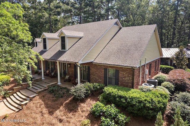 rear view of house featuring brick siding, cooling unit, and a shingled roof